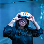 Photo of a person, Emmie Lin, holding VR goggles on their head