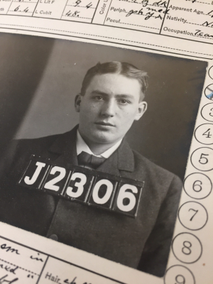 A medium close-up photograph of a man in a suit with an identifying number in large block letters and numbers on top of the suit