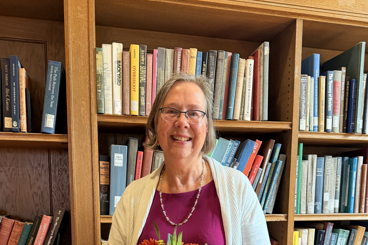 Photo of Sue Cardinal standing in front of a bookshelf holding flowers