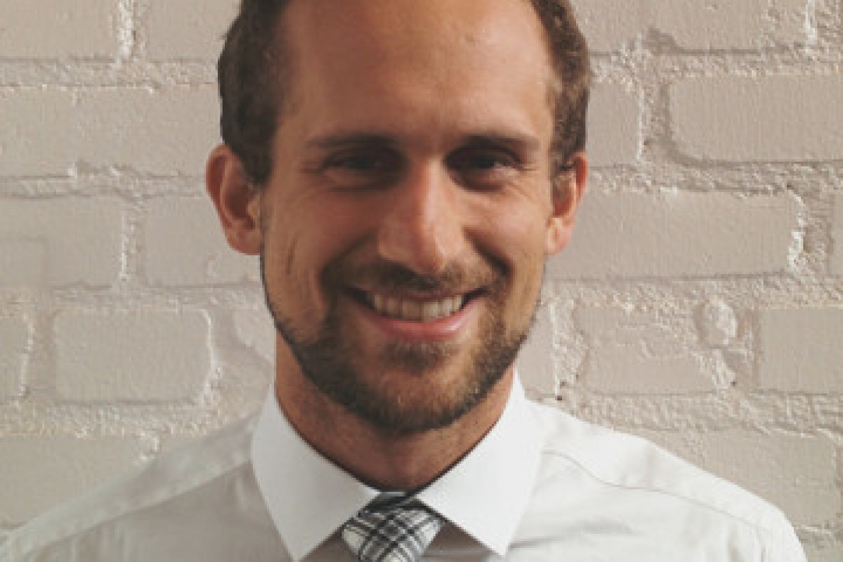 Photo of Andrew White standing against a white brick wall