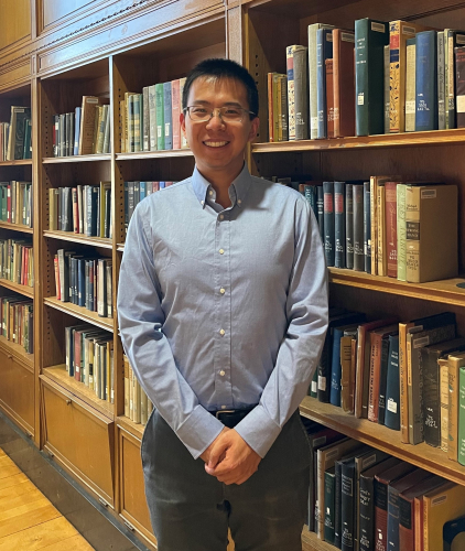 Lipeng Chen next to a book shelf in Welles-Brown Room