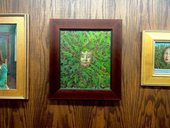 A framed painting, at center a face with green leaves growing out of it