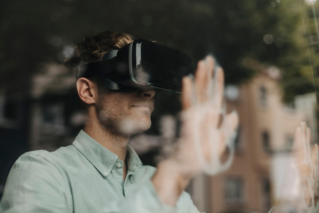 A man wearing a virtual reality headset touches a glass surface with both hands.