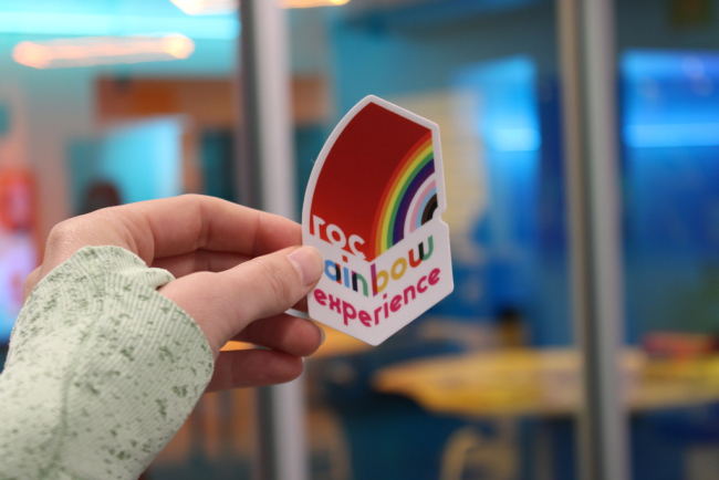 Person holding a sticker for the Roc Rainbow Experience.