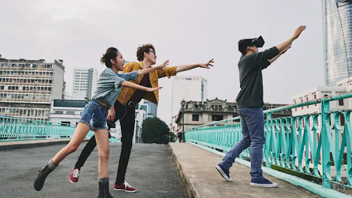 Person wearing a VR headset wanders near a bridge and two people dramatically try to stop the VR user from going off the side.