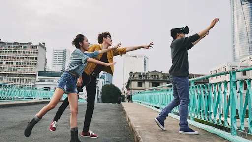 Person wearing a VR headset wanders near a bridge and two people dramatically try to stop the VR user from going off the side. 