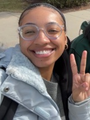 A person, Serenity Henlon, taking a selfie of themselves with their hand showing a peace sign